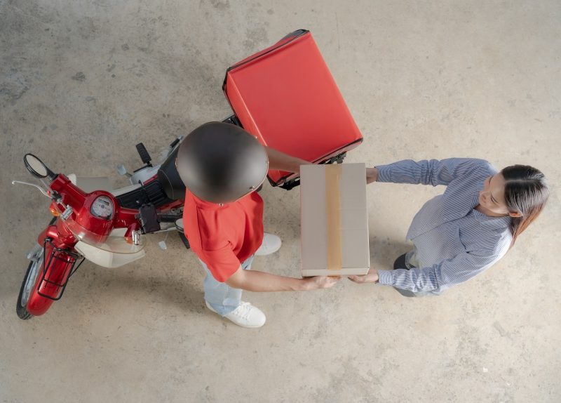 Top-down view captures the moment a scooter courier delivers a package to a waiting customer, symbolizing efficient urban delivery services and the gig economy