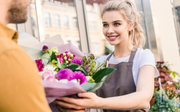 smiling attractive florist giving bouquet to customer near flower shop